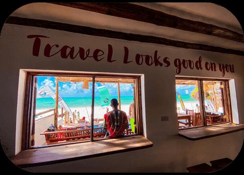 Inside Helio Capitano with the words 'Travel looks good on you' above windows framing Paje Beach