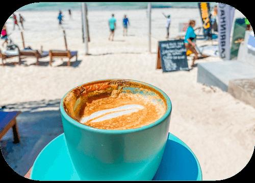 A beach cappuccino held up against Paje's white sand and kitesurfers