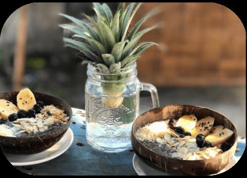 Two coconut-shell smoothie bowls with banana and chia on a beachside table
